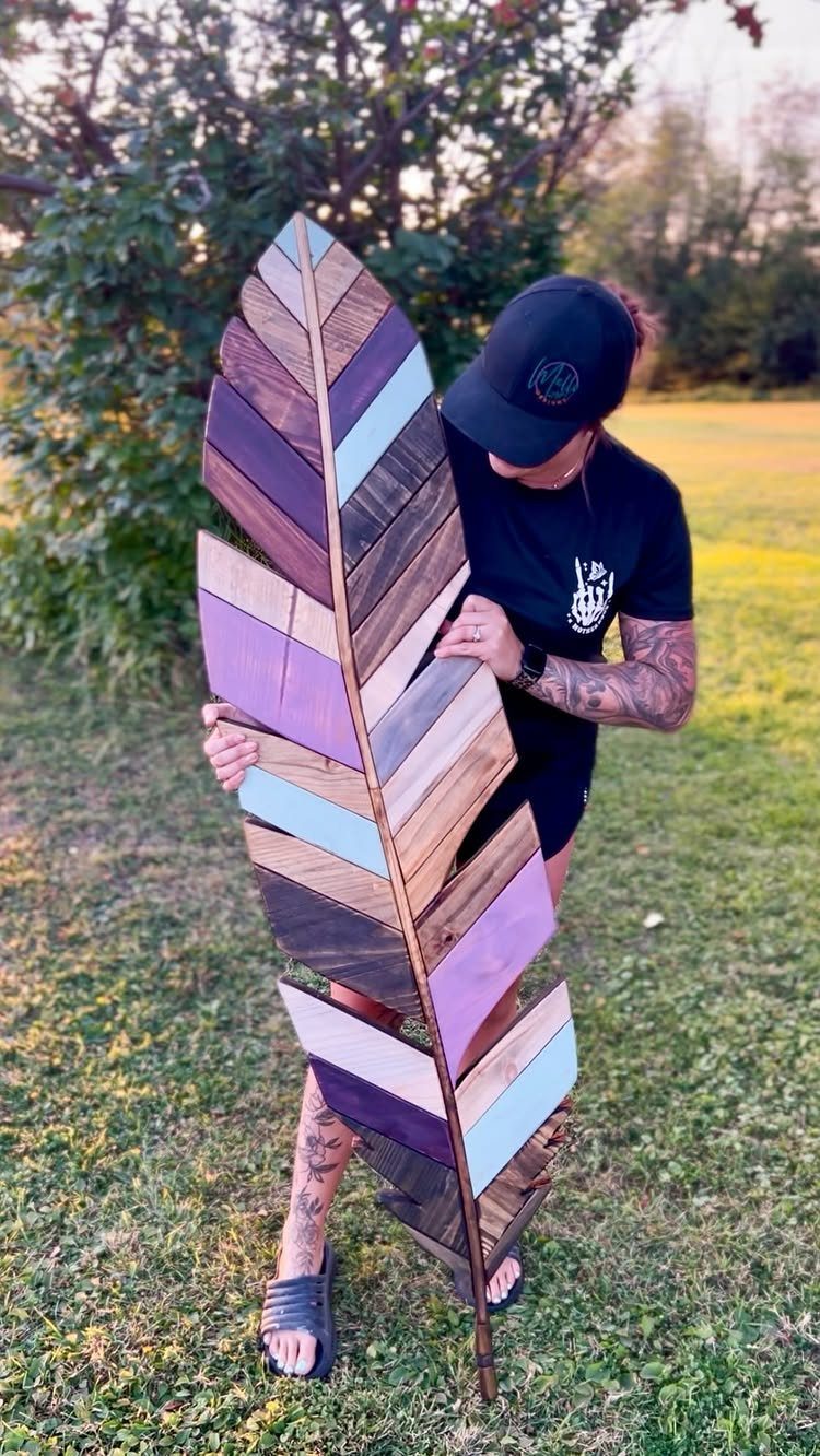 Wood Piece Art Ideas: 25 Designs for Walls and Shelves 14 Feather-shaped wooden wall art with purple and blue slats held by a person outdoors.