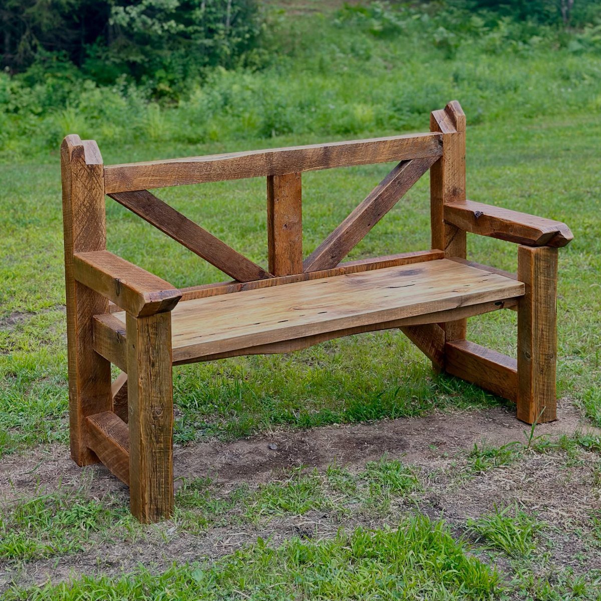 Rustic wooden X-back bench sitting on a green lawn with a dirt path.