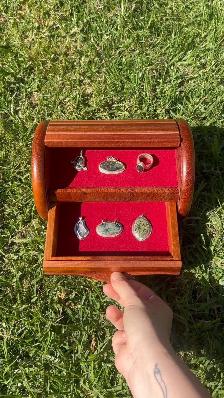 Wooden jewelry box with red velvet interior holding rings and pendants on green grass