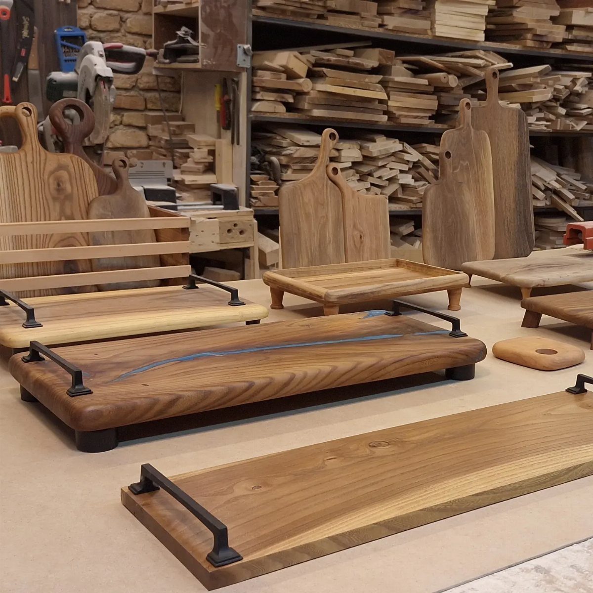 Wooden serving trays with black handles and cutting boards in a woodworking shop