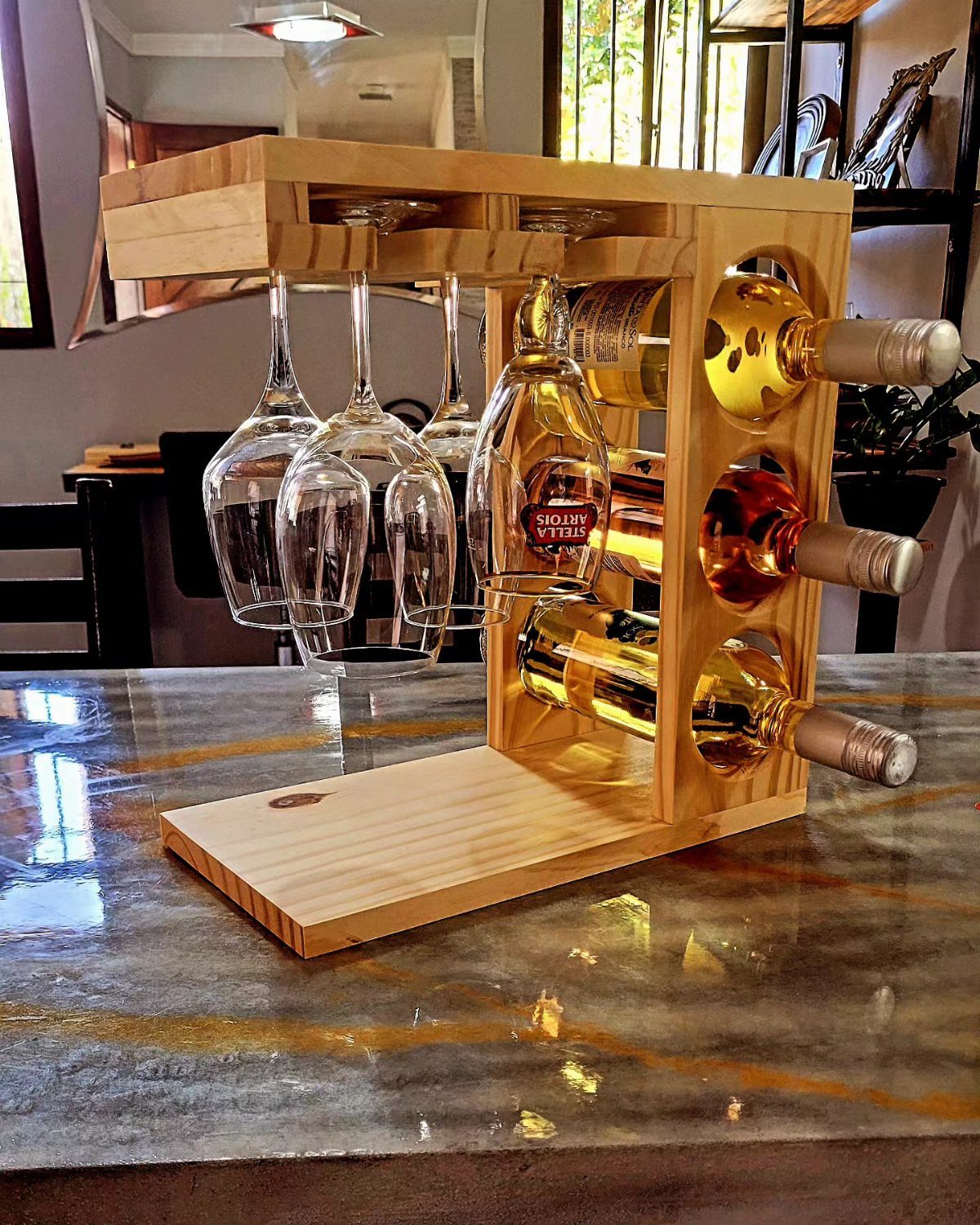 Wooden wine rack holding wine bottles and hanging glasses on a marble counter.