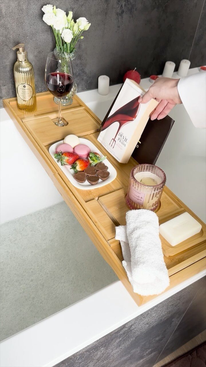 Wooden bath caddy across a tub with wine, chocolates, a candle, and a book.