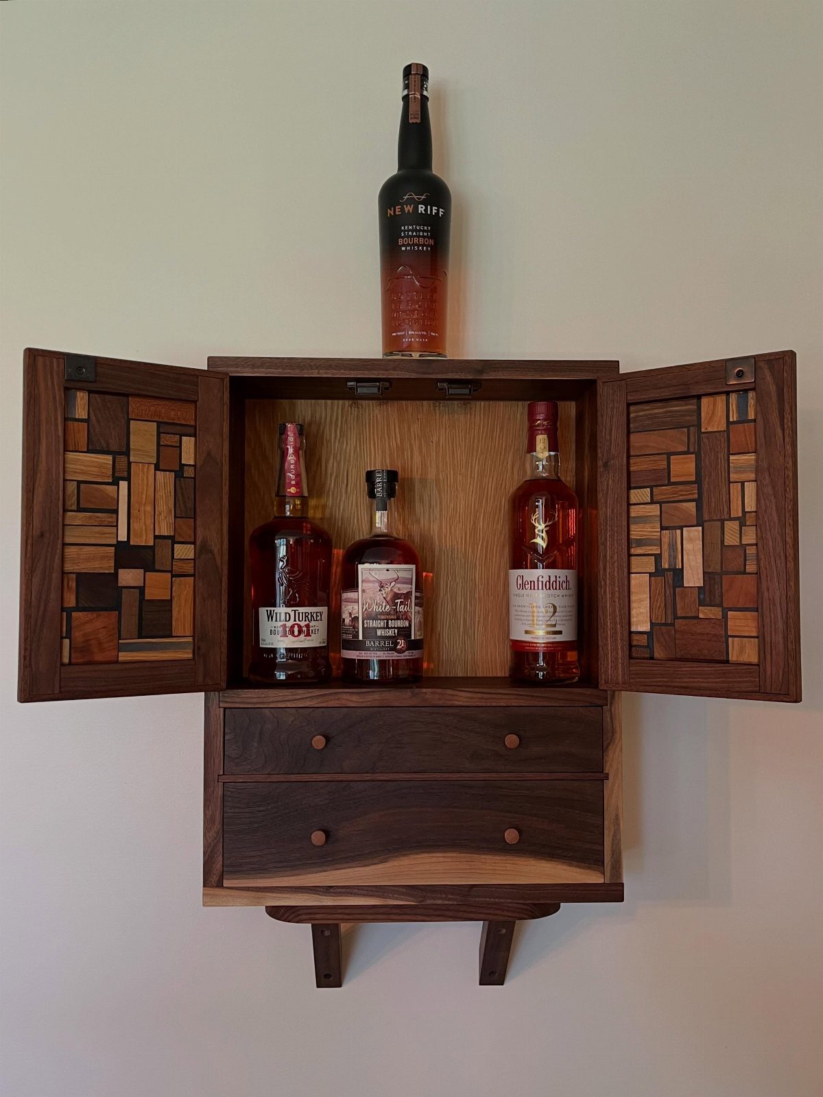 18 Wood Projects with Plans for Every Skill Level 11 Wooden whiskey cabinet with mosaic doors and drawers holding several liquor bottles.