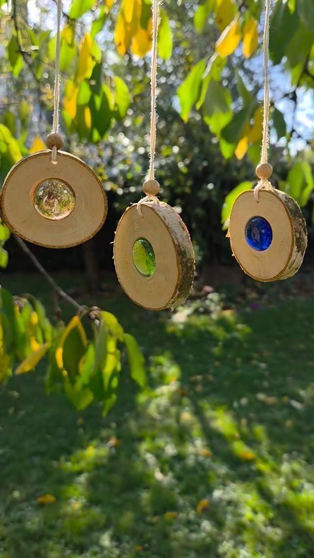 Three wood slice ornaments with colorful glass gems hanging from a tree branch.