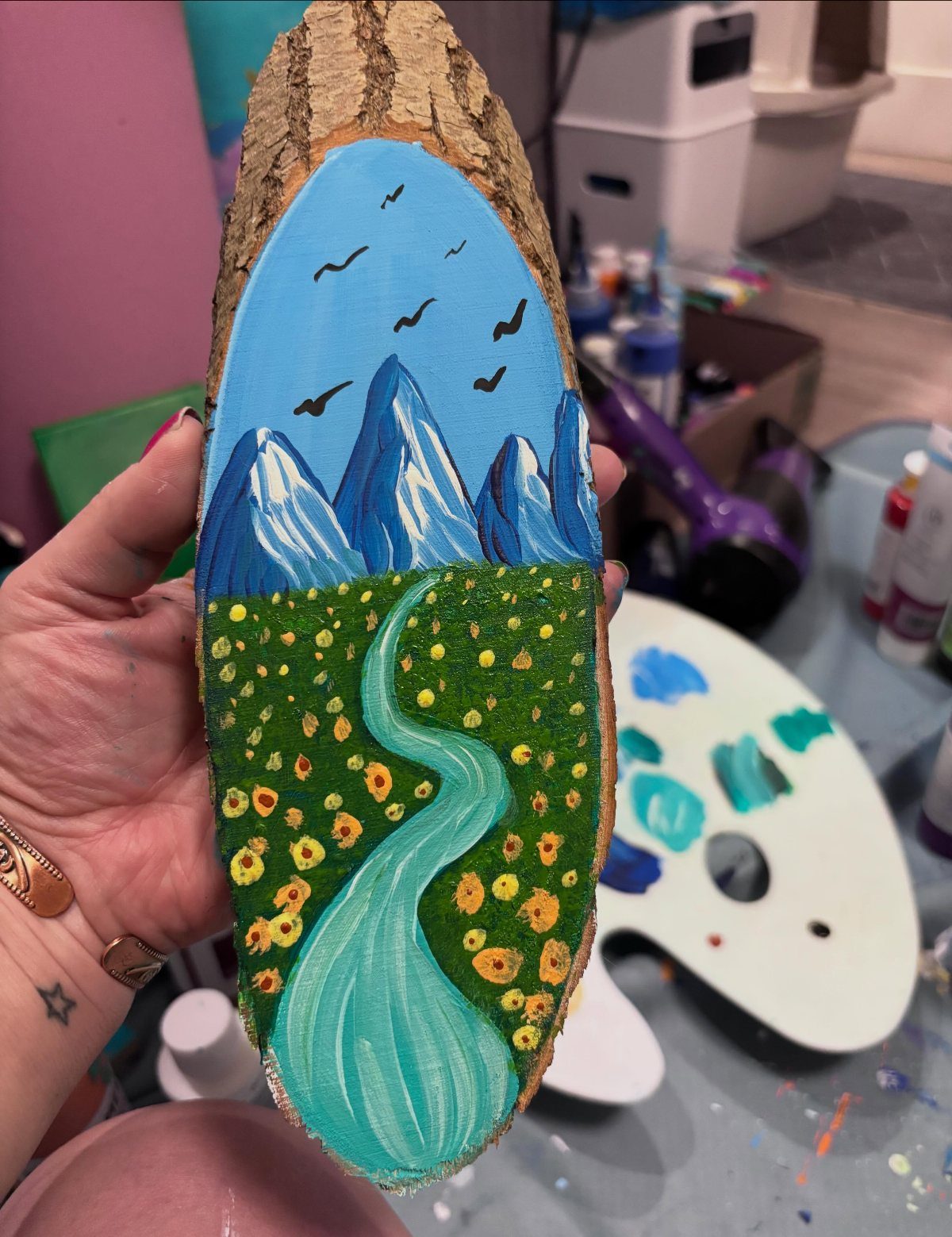 Painted landscape of mountains and a river on a natural wood slice