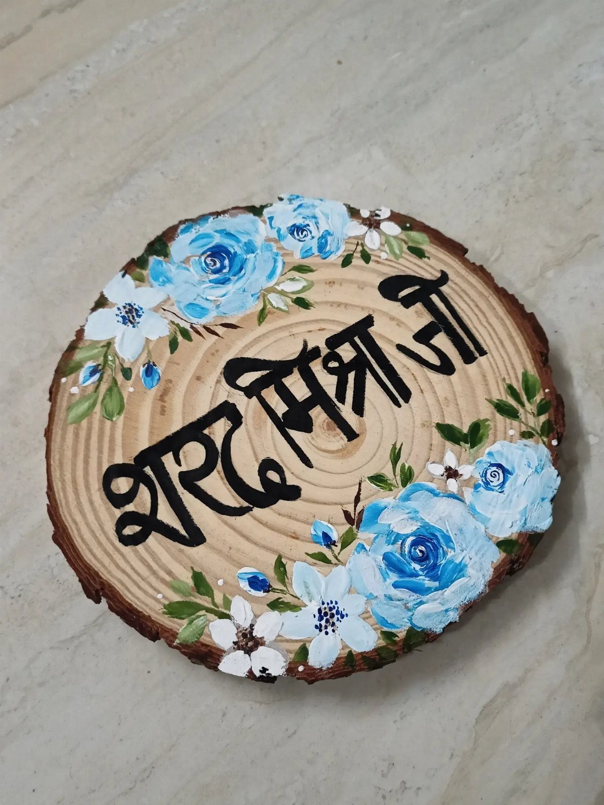 Wood slice art featuring painted blue roses and black Hindi calligraphy on natural wood.