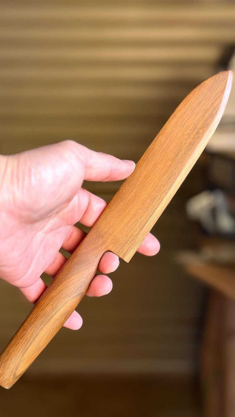Hand holding a carved wooden knife made from light brown grained wood.