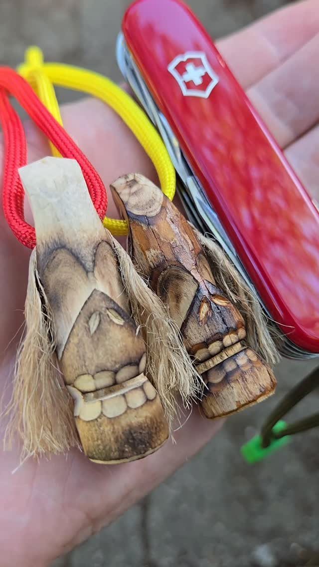 Two small hand-carved wooden tiki figures and a red Swiss Army knife in a hand.