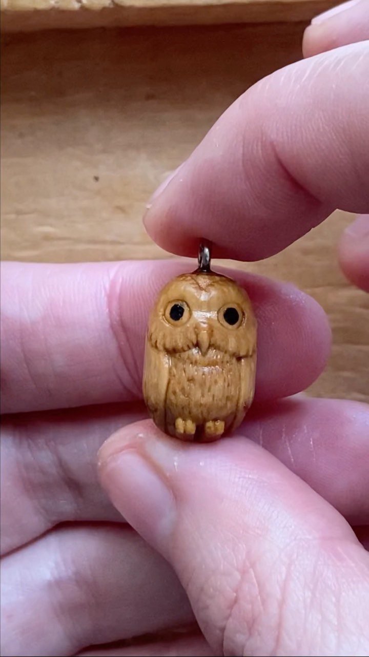 Small hand-carved wooden owl pendant held between two fingers.