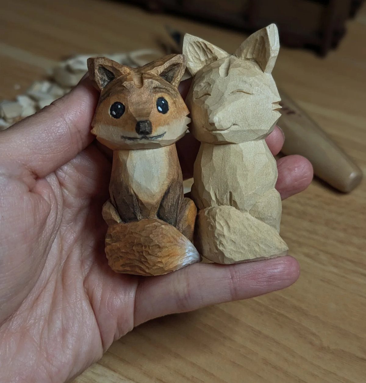 Two small whittled wooden foxes, one painted and one natural, held in a hand.