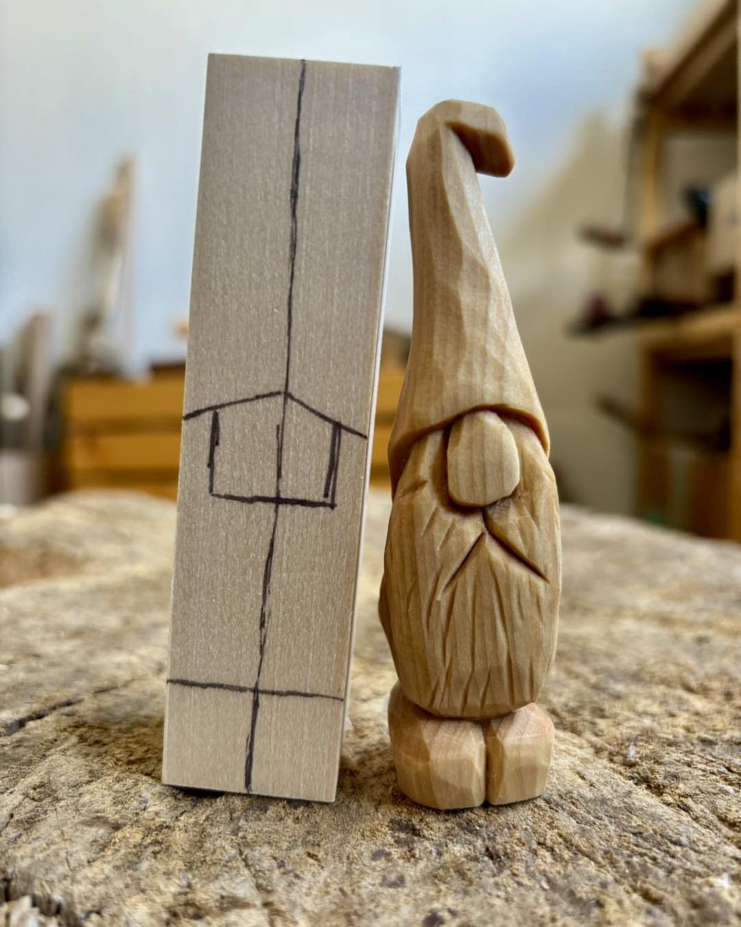 Hand-carved wooden gnome standing next to a wood block with carving guidelines.