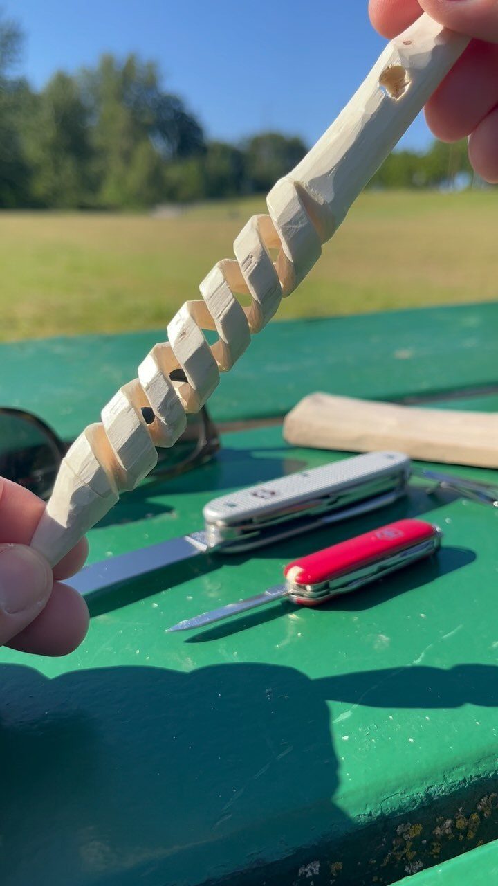 Hand-carved wooden spiral held above a green table with two pocket knives.