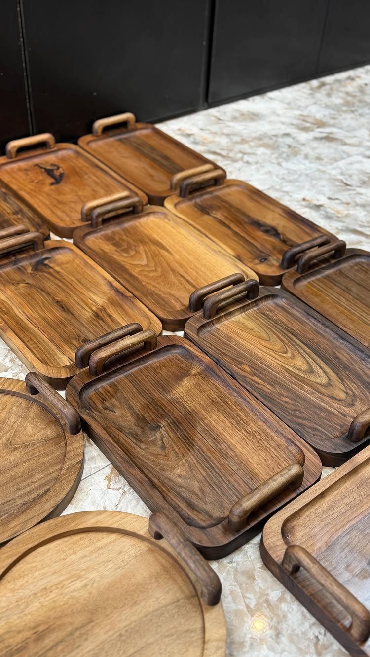 Polished dark brown wooden trays of various shapes arranged on a marbled floor.