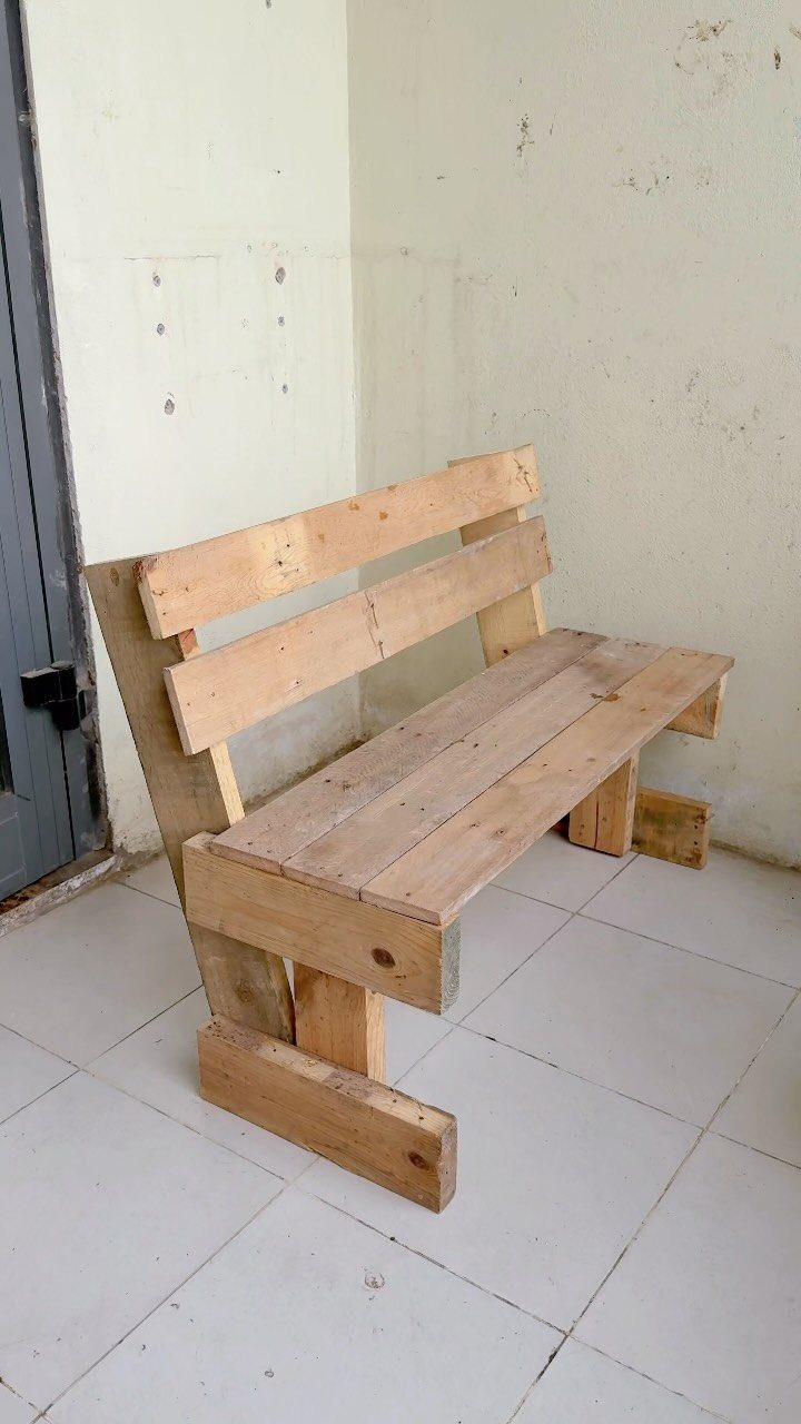 Handmade wooden bench made from light-colored pallet wood against a white wall