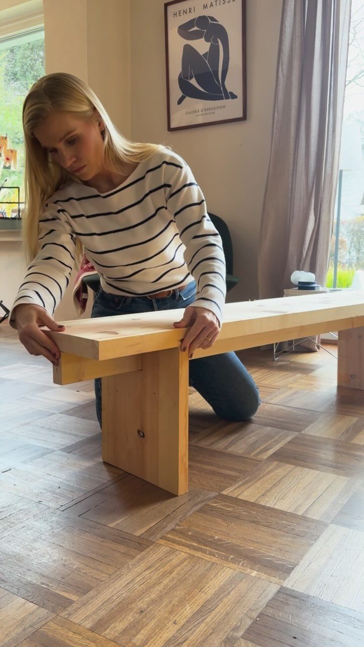 Woman assembling a simple light wood bench on a parquet floor.