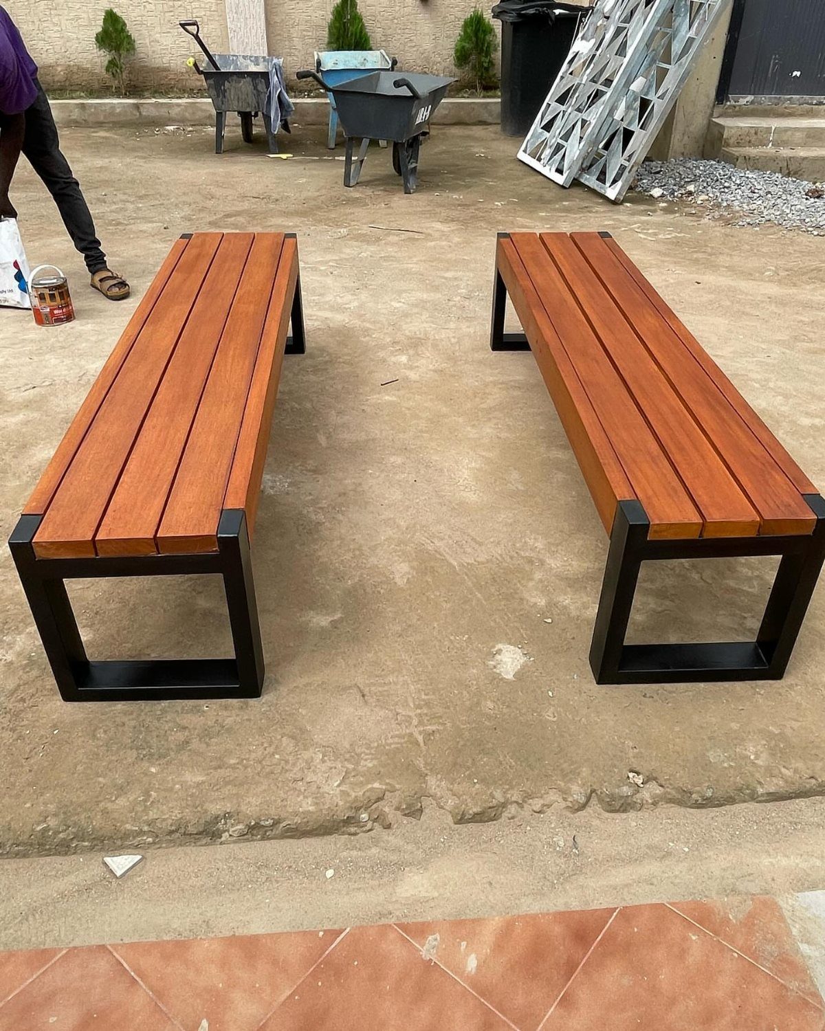 Two long wooden benches with black metal legs on a concrete surface.