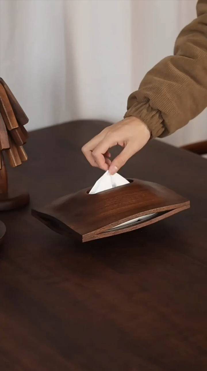 7 Wooden Box Designs for Jewelry, Tissue and Storage 6 Curved dark brown wooden tissue box on a table with a hand pulling a tissue.