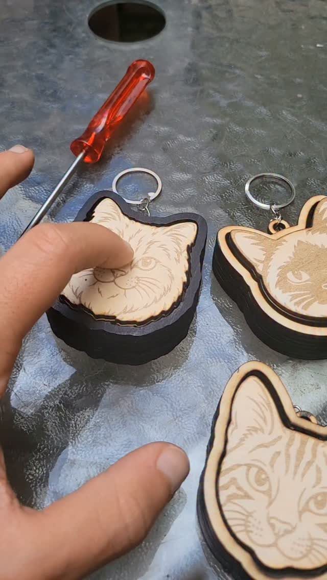 Wooden Cat Face Ideas: 5 Cutouts, Carvings and Wall Art 1 Wooden cat head keychains with engraved features and dark borders on a glass table.