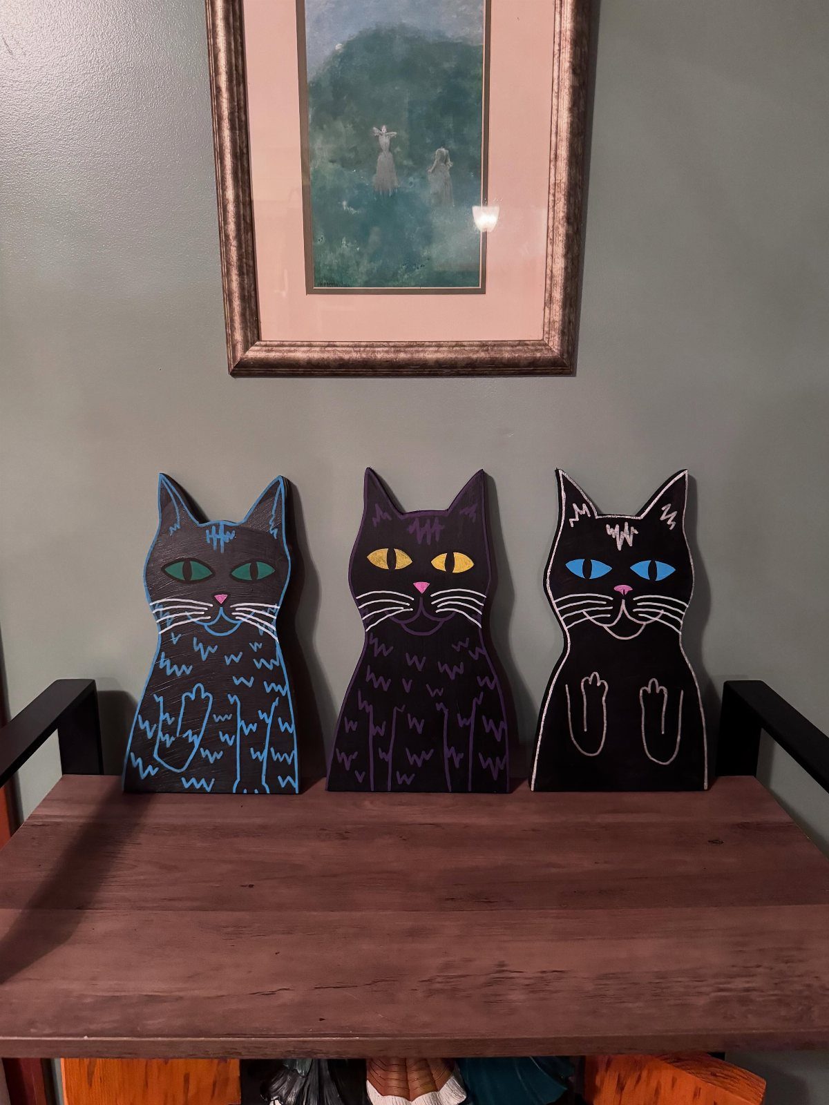 Wooden Cat Face Ideas: 5 Cutouts, Carvings and Wall Art 3 Three painted wooden cat cutouts in dark colors standing on a wooden shelf.