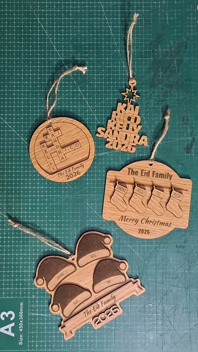 Wooden Christmas ornaments with engraved names and stockings on a green cutting mat.
