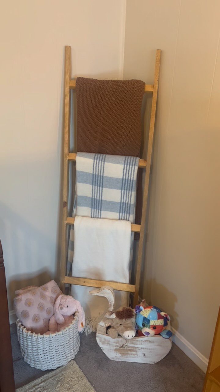 Wooden blanket ladder leaning against a wall holding three folded blankets in a room.