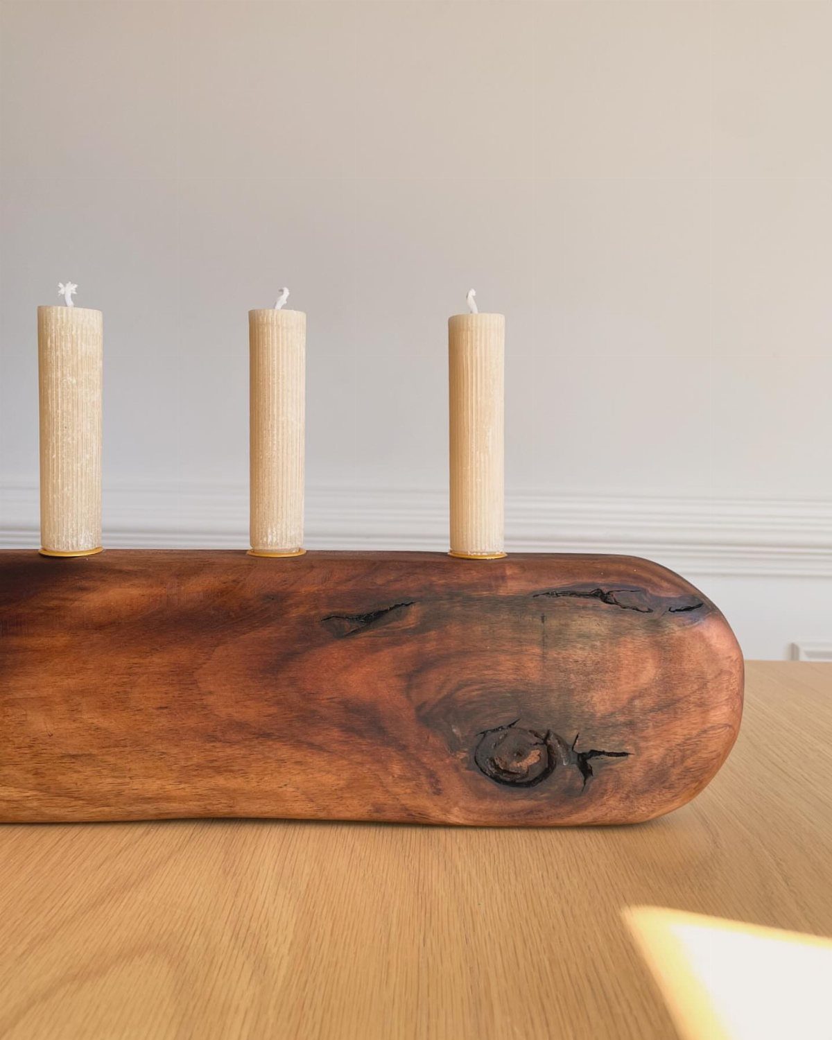 Three beige pillar candles held in a polished dark brown natural wood log base.