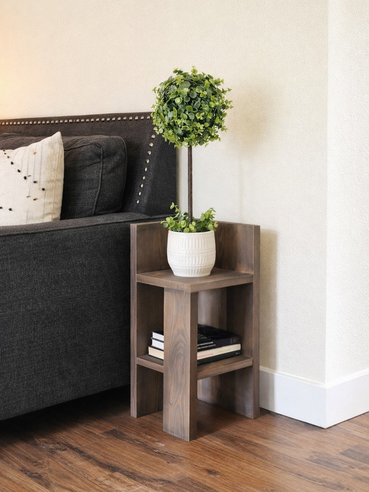 Brown wooden end table with a potted plant and books next to a sofa.