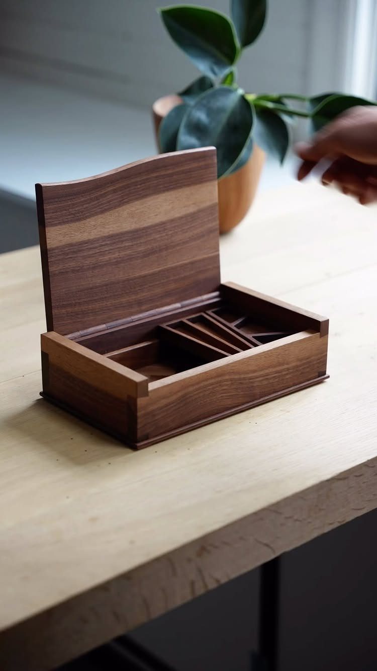 Wooden jewelry box with a curved lid and compartments on a light table.