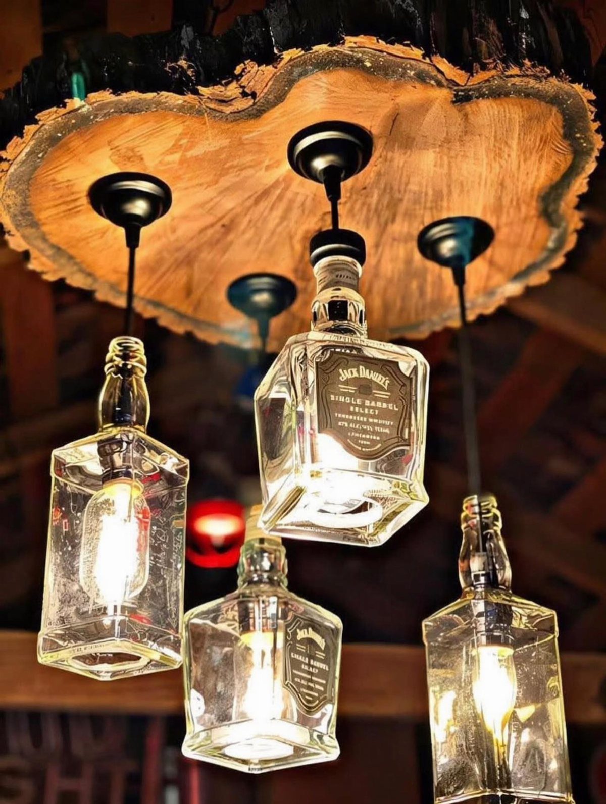 Whiskey bottle pendant lights hanging from a rustic natural edge wood slab.