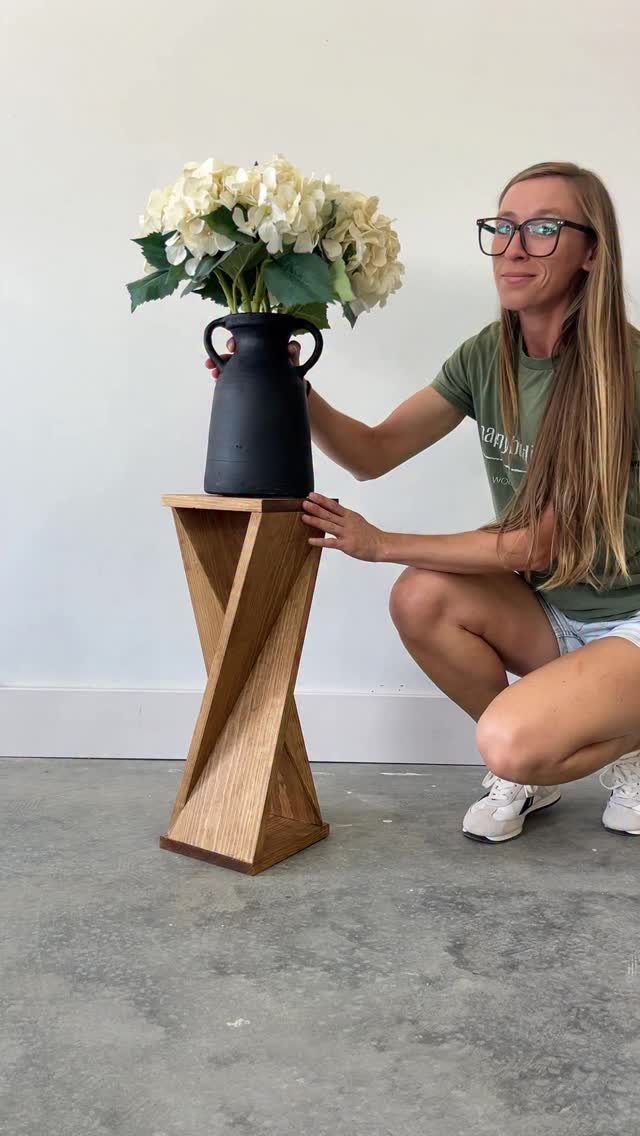 Twisted wooden pedestal stand holding a black vase with white hydrangea flowers.