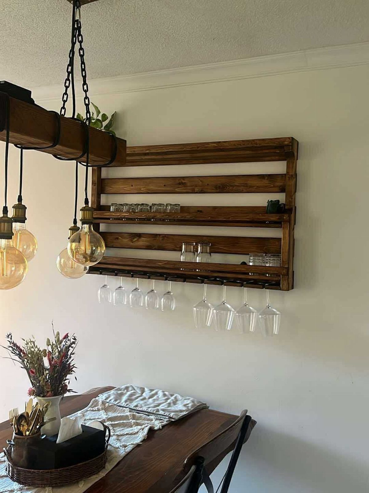 Wooden wall-mounted wine rack holding several clear hanging wine glasses against a white wall.