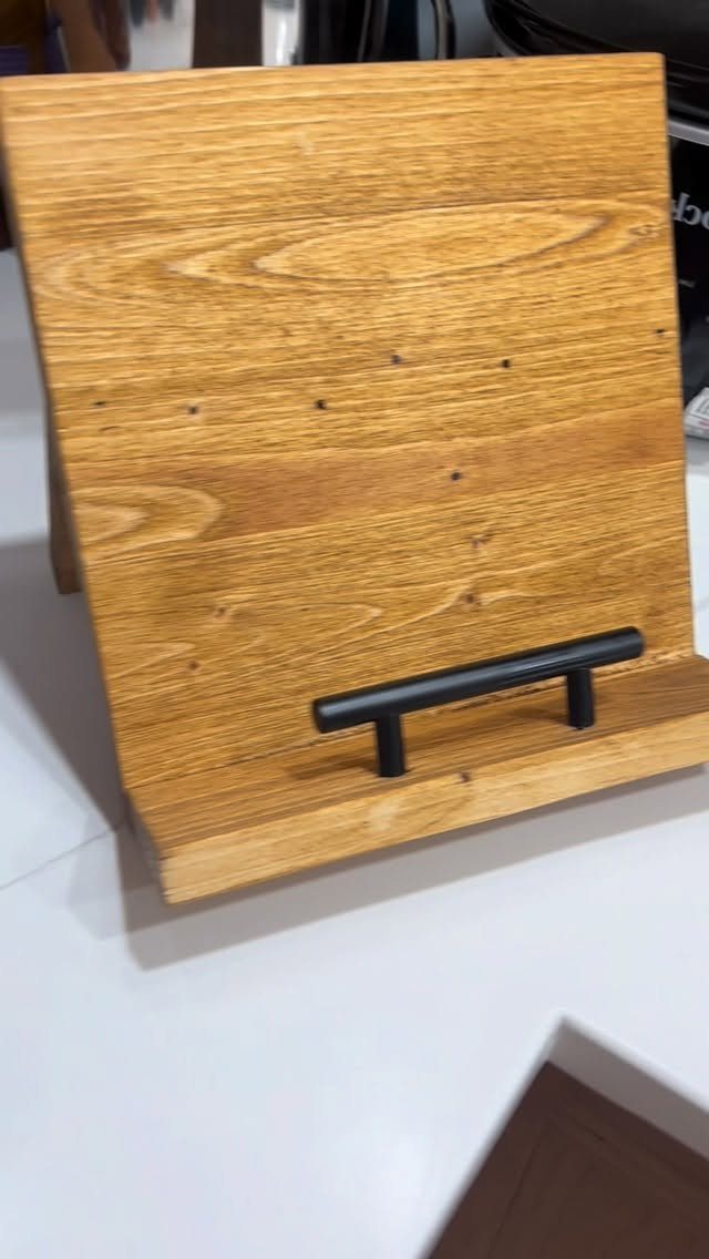 Wooden cookbook stand with a black metal holder on a white countertop.