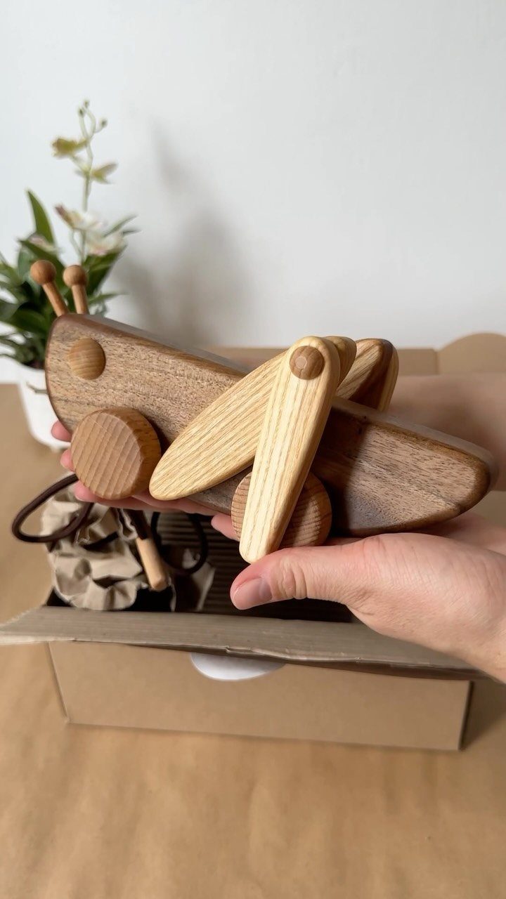 Handcrafted wooden toy airplane held over a cardboard shipping box.