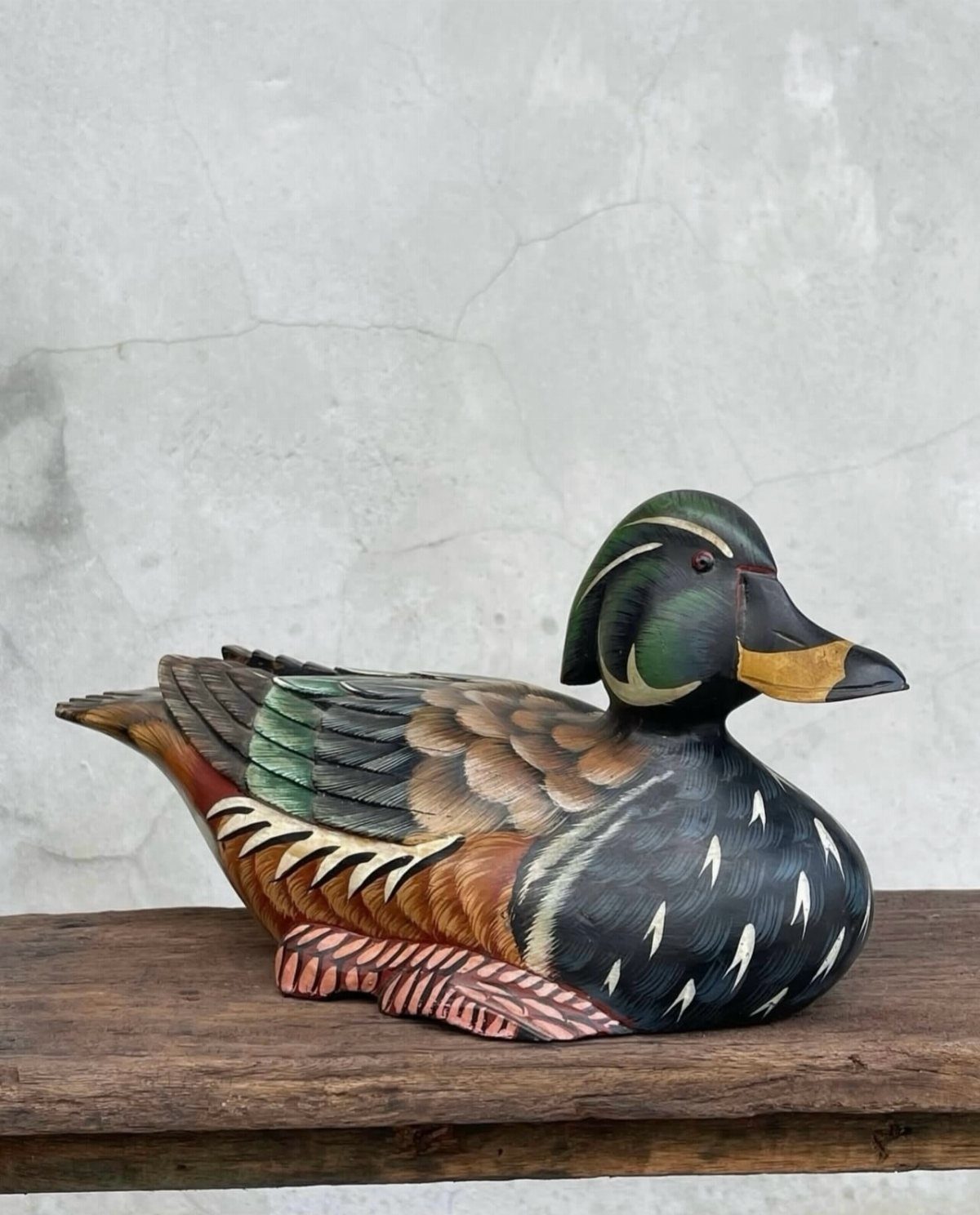 7 Ideas for Wooden Duck Carving, From Decoys to Flight Poses 4 Wooden duck carving with colorful painted plumage resting on a rustic wooden beam