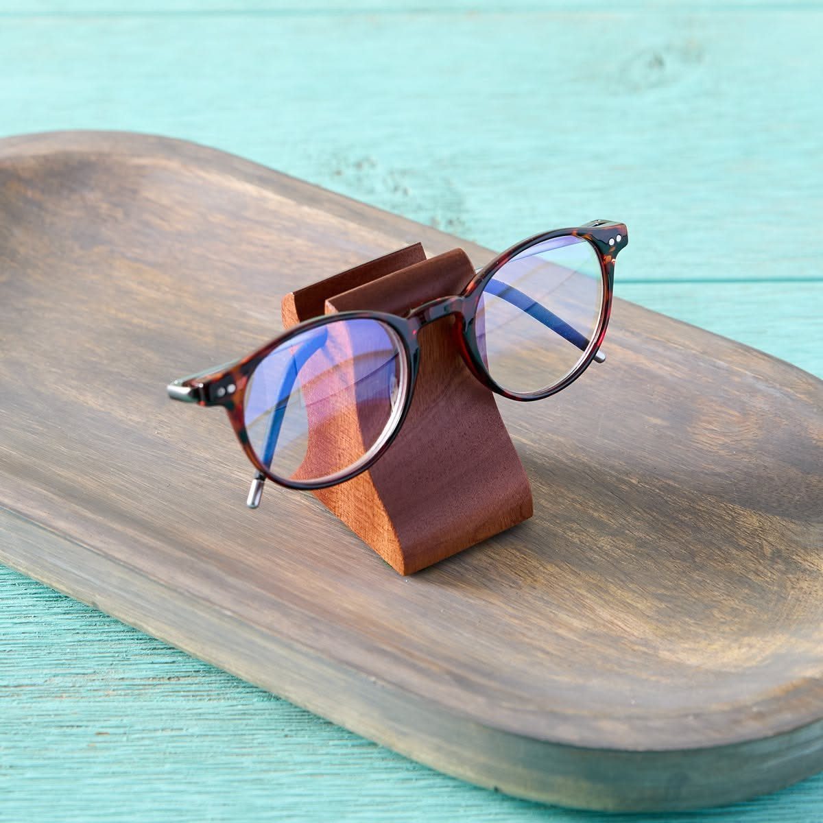 Wooden Glasses Holder: 10 Ideas for Every Desk 5 Dark-rimmed glasses on a brown leather holder atop a curved wooden tray.