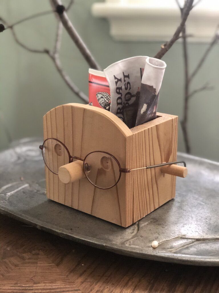 Wooden Glasses Holder: 10 Ideas for Every Desk 9 Wooden block glasses holder with a nose peg holding round spectacles and newspapers.