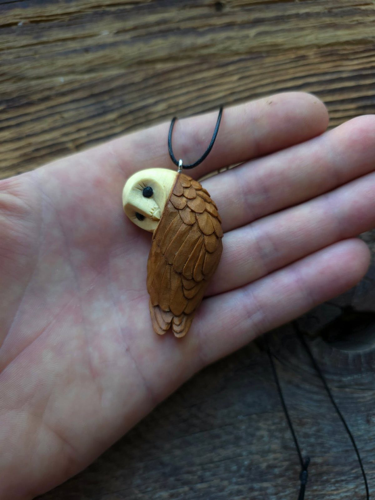 Small hand-carved wooden owl pendant resting in the palm of a hand