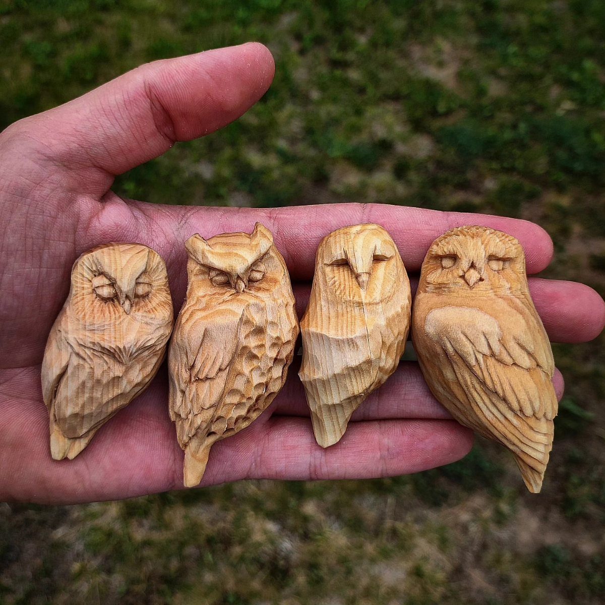 Four hand-carved wooden owl figurines resting in an open palm over green grass.