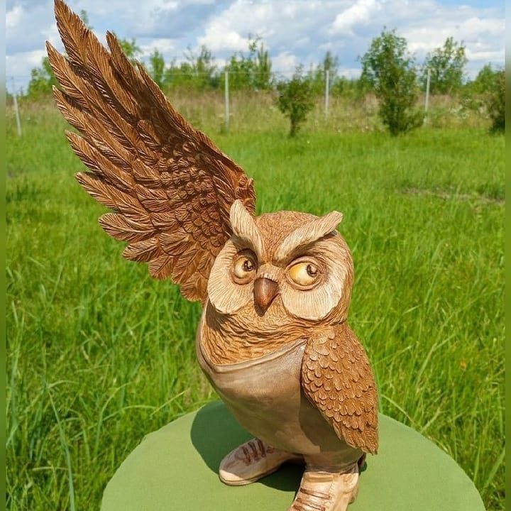 Wooden owl carving wearing an apron and shoes in a grassy outdoor setting.