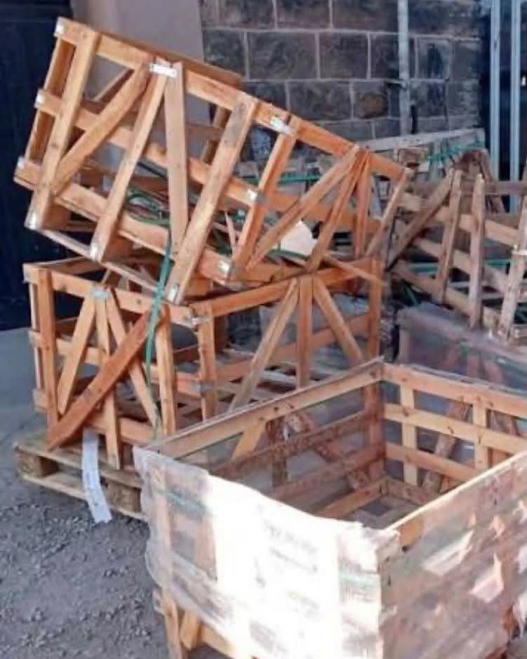 Wooden pallet crates and frames stacked against a grey stone wall outdoors.
