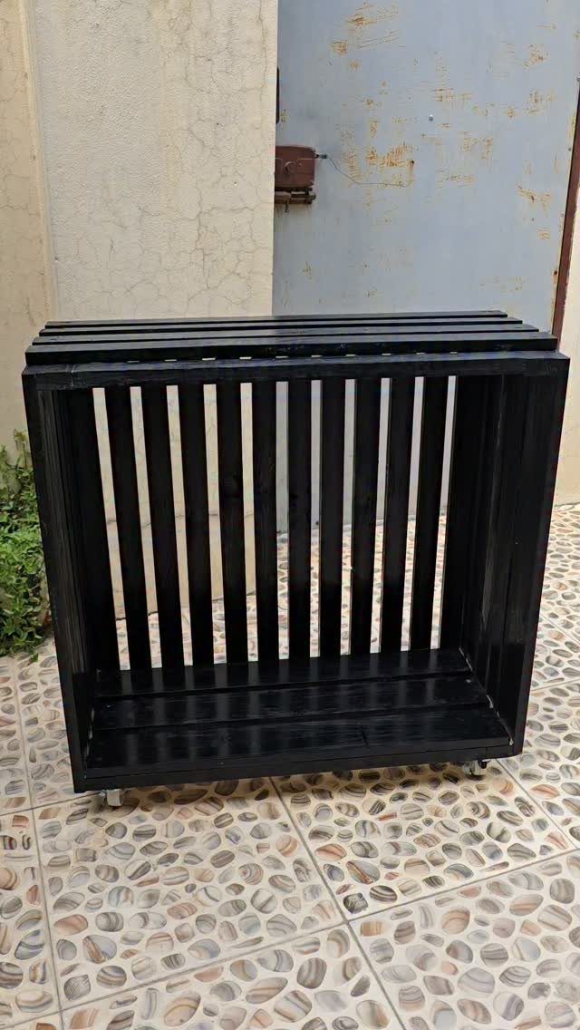 Black painted wooden pallet crate with vertical slats on a tiled floor.