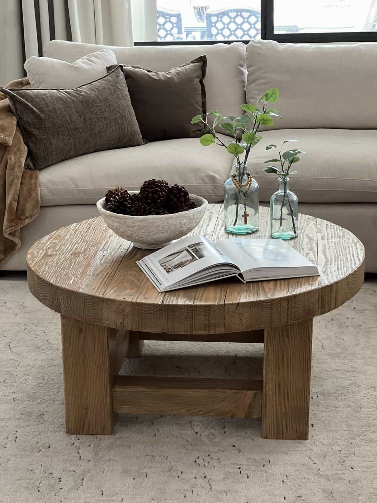 9 Woodworking Coffee Table Ideas for Every Skill Level 6 Round chunky wooden coffee table with a bowl of pinecones and greenery in a living room