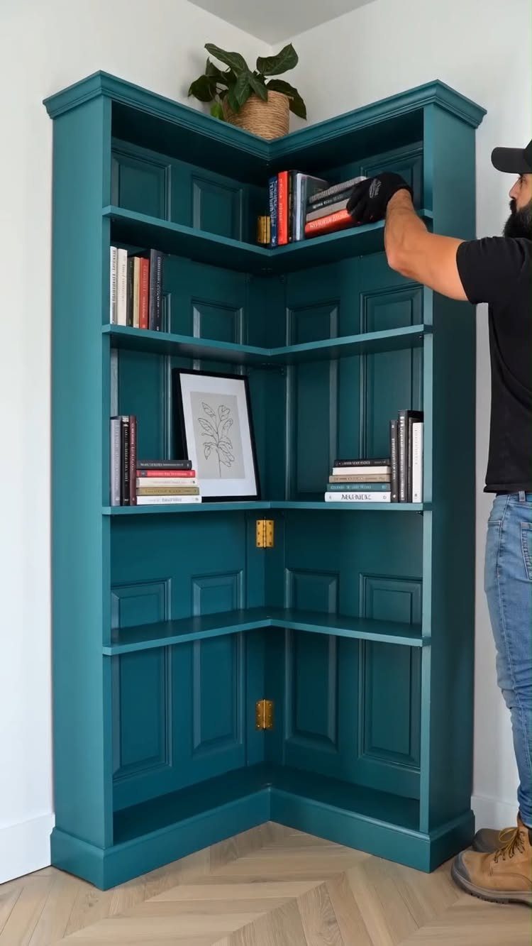 Teal corner bookshelf with paneled backing and books being organized by a man.