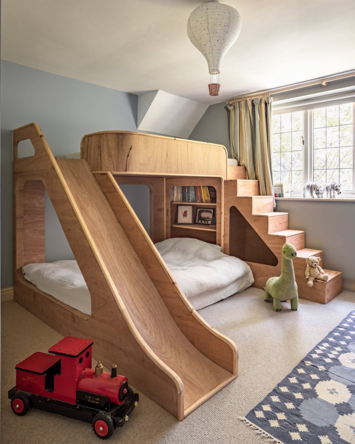 Wooden bunk bed with a built-in slide and stairs in a child's bedroom.