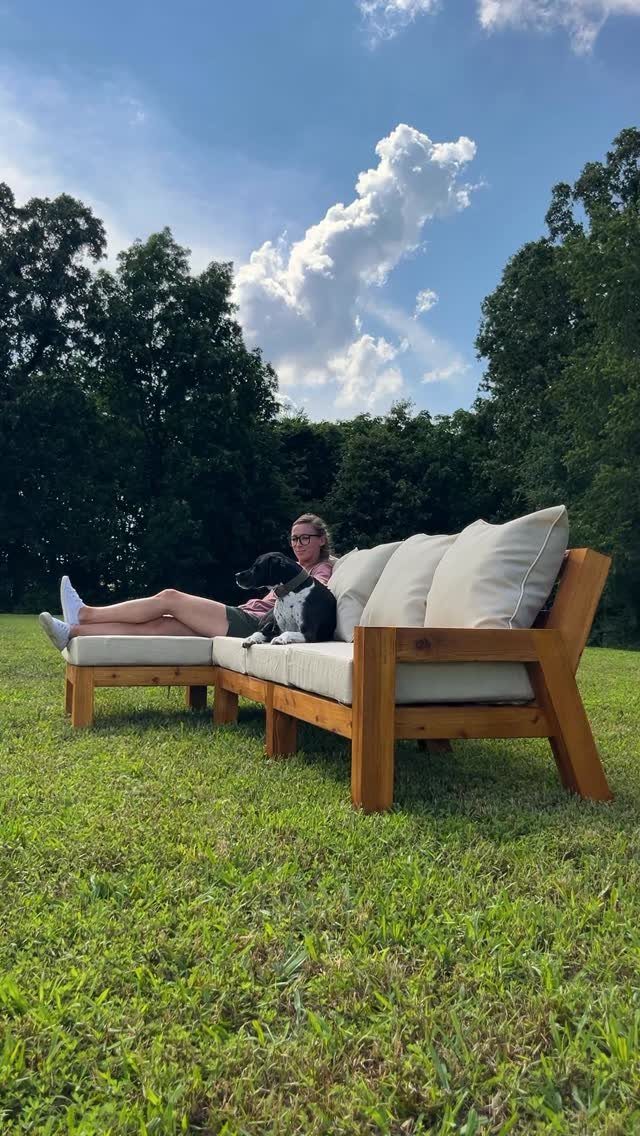 Wooden outdoor sectional sofa with beige cushions on a green lawn under a blue sky.