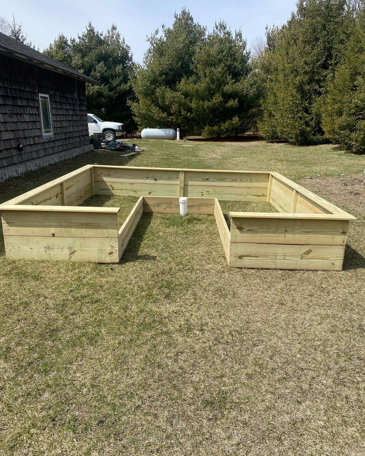 U-shaped raised garden bed made of light wood planks on a grassy lawn.