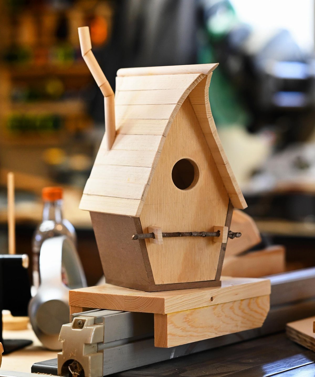 14 Woodworking Ideas to Make Money From Your Shop 7 Wooden birdhouse with a curved roof sitting on a workbench in a workshop.