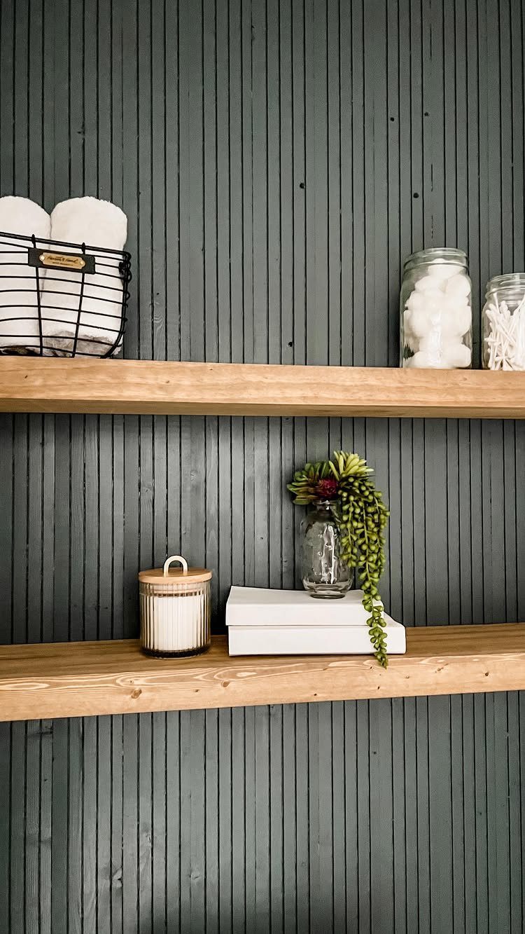 14 Woodworking Ideas to Make Money From Your Shop 2 Two light wood floating shelves on a dark grey slatted wall with decor.