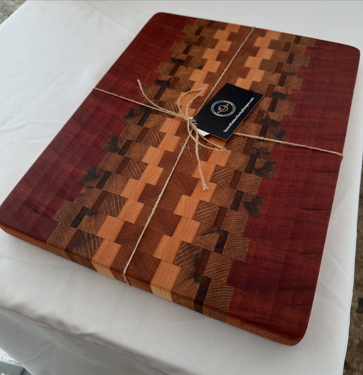 14 Woodworking Ideas to Make Money From Your Shop 4 Wooden cutting board with a red and brown mosaic pattern tied with twine.