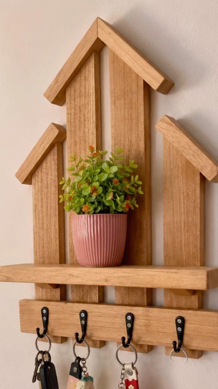 Wooden house-shaped key holder with a small shelf, potted plant, and black hooks.
